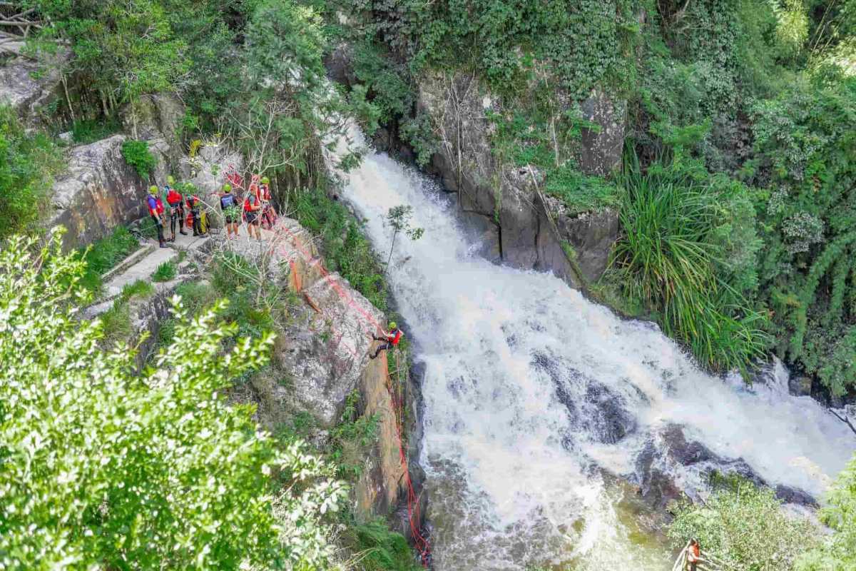 Upper View of Canyoning Adventure at Datanla Waterfalls Overhead view showing adventurers rappelling down a waterfall with lush forest around Datanla Waterfalls