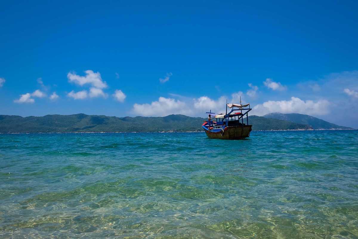 Traditional wooden boat in Van Phong Bay waters A lone wooden boat floats in crystal-clear waters with distant mountains in Van Phong Bay