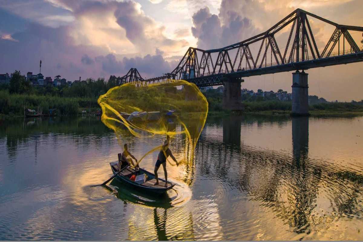 Vibrant Sunset Over Long Bien Bridge Long Bien Bridge framed by vibrant sunset colors reflecting on the water