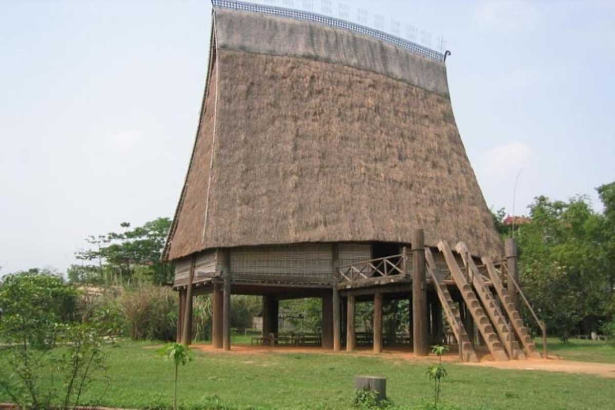 Vietnam Museum of Ethnology Hanoi traditional stilt house exterior Vietnam Museum of Ethnology Hanoi traditional stilt house with thatched roof and wooden stairs in lush green setting.