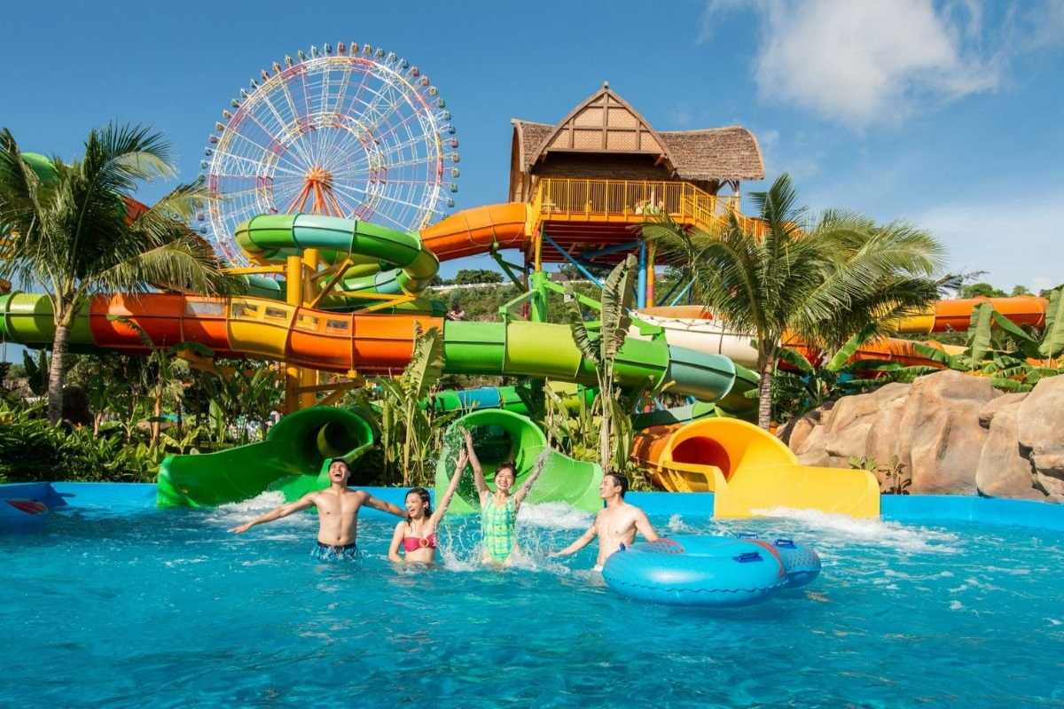 Families Playing in VinWonders Water Park Family splashing in the pool with colorful slides and ferris wheel in the background at VinWonders Nha Trang
