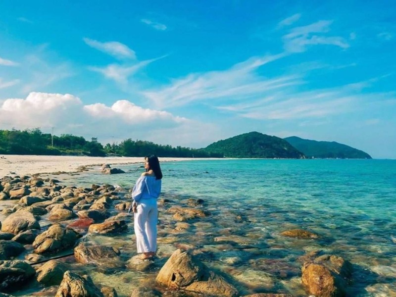 Visitor standing on rocky shore with clear blue waters at Minh Chau Beach