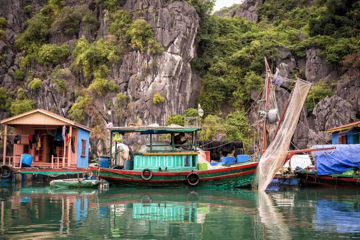 Vung Vieng Fishing Village traditional fishing boat Traditional fishing boat moored at Vung Vieng Fishing Village with lush limestone cliffs in the background