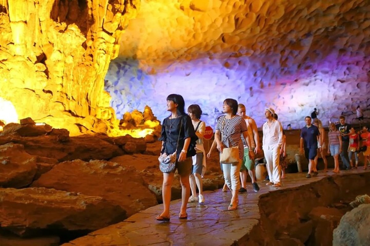 Group of tourists walking along a path inside Sung Sot Cave, Halong Bay, with brightly lit limestone formations around them.