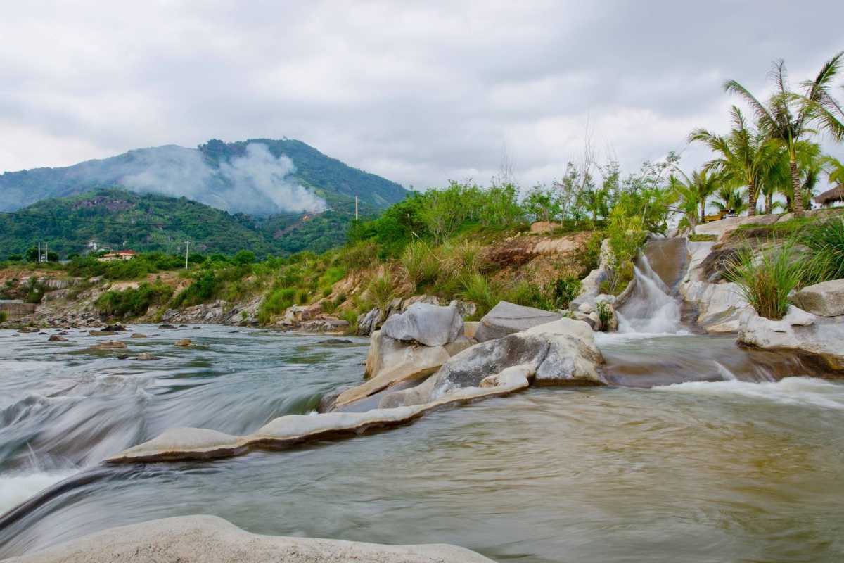 Stream slide and mountain view at Waterland Water flows down a built slide beside the stream, with misty mountains in the background at Waterland Thach Lam.