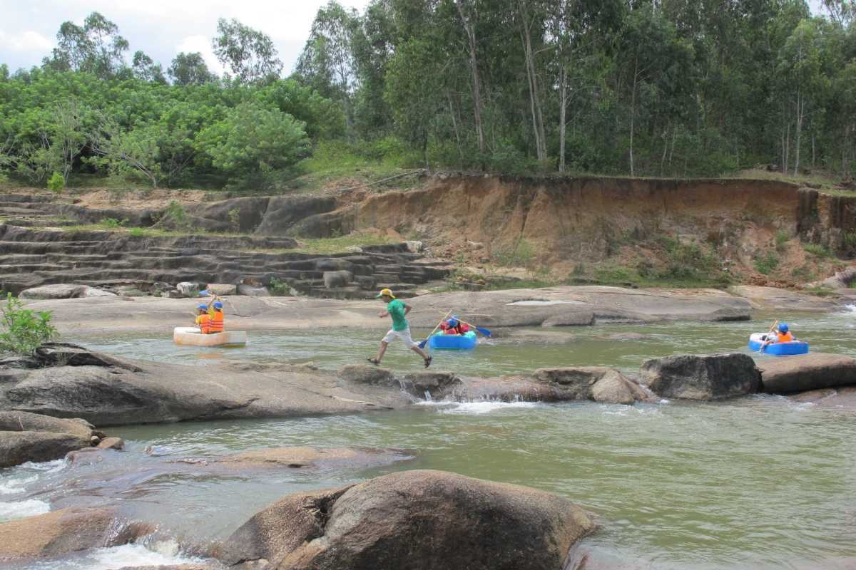 Children and parents tubing along the rocky stream at Waterland Thach Lam with safety gear.