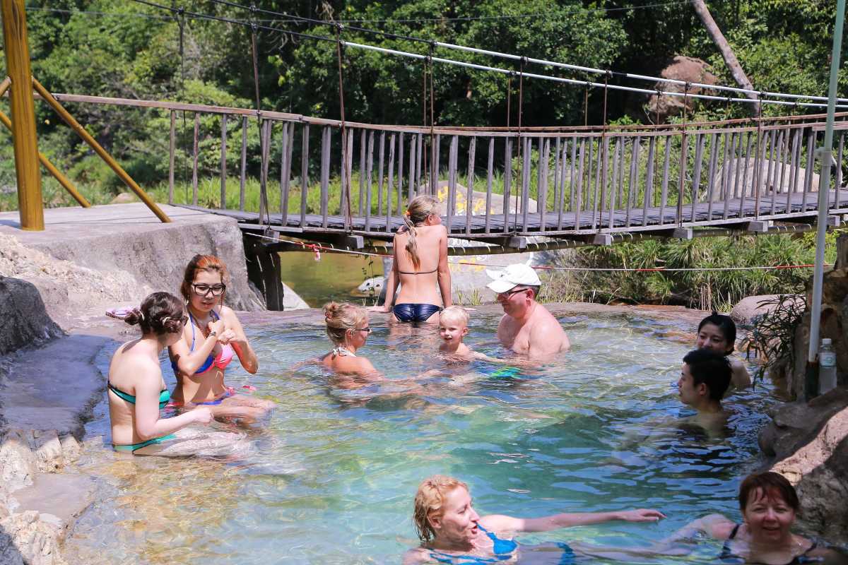 Yang Bay Waterfall hot springs experience Visitors enjoying the natural hot spring pool at Yang Bay Waterfall with a wooden bridge in the background