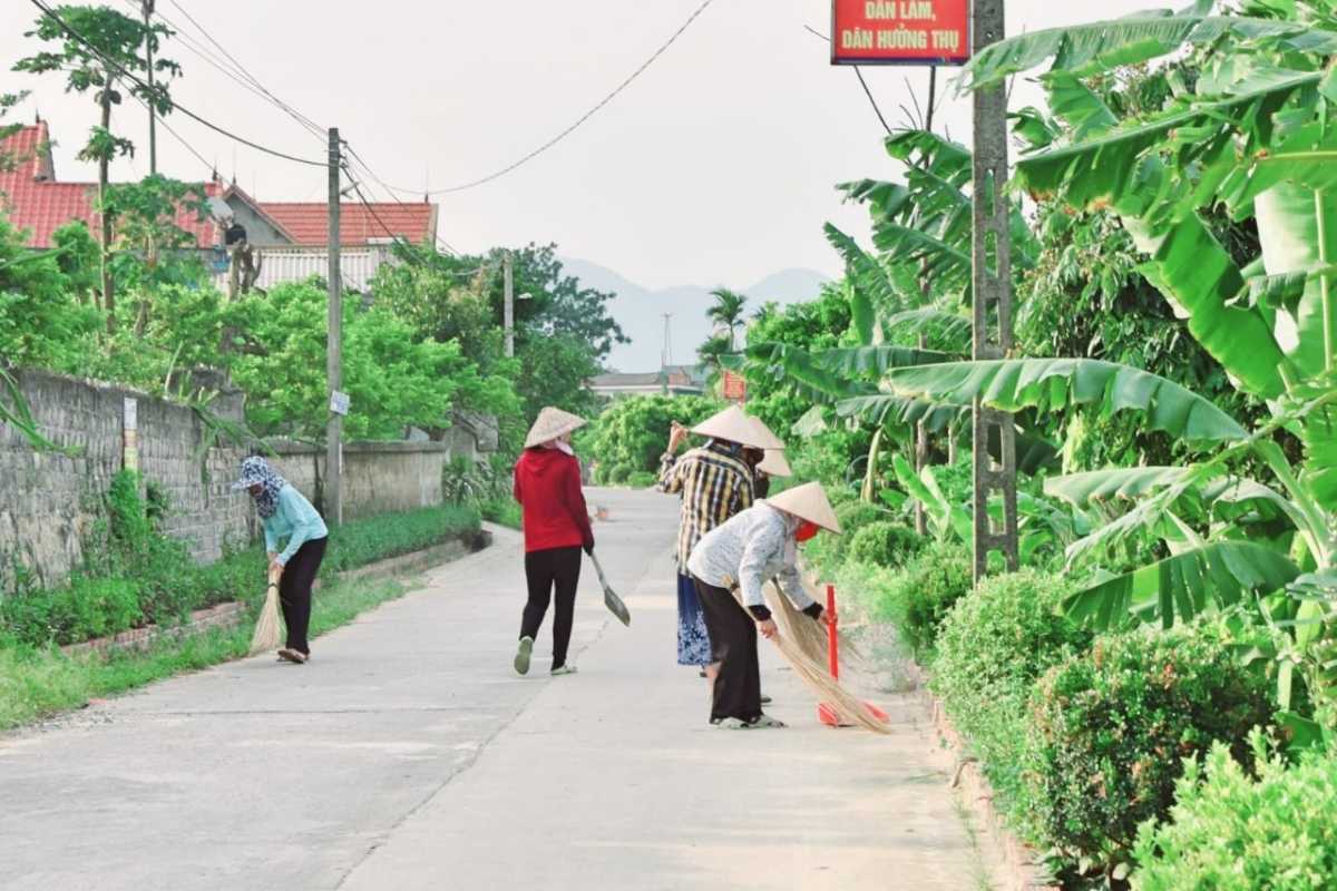 Community Cleaning Effort in Yen Duc Village Local residents in traditional hats sweeping the streets of Yen Duc Village, showing community spirit.