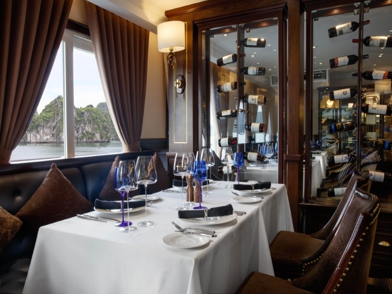 Window-side table at Le Marin Restaurant aboard Paradise Elegance Cruise with wine storage and bay views.