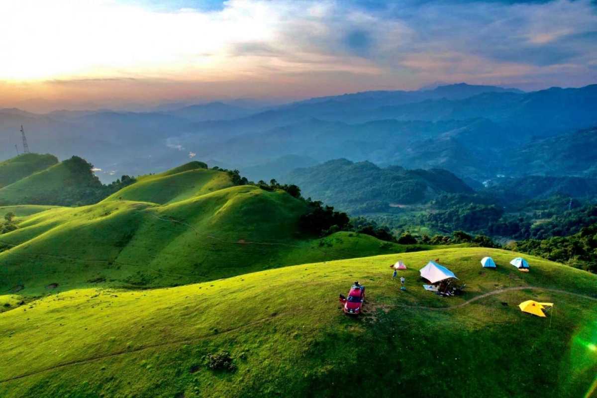 Bac Giang Travel Sunset Over Rolling Green Hills Bac Giang Travel captures a scenic sunset casting warm light on rolling green hills with camping tents and vehicles