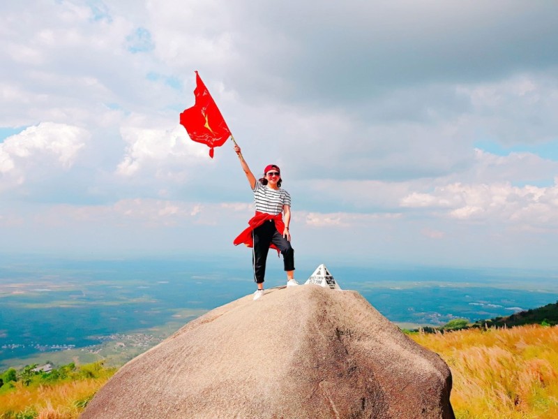 A hiker raising a flag at the summit of Chua Chan Mountain in Dong Nai, showcasing the triumph of the climb