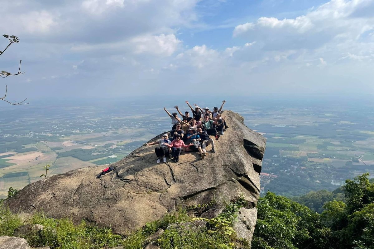 A group of hikers celebrating at the top of Chua Chan Mountain in Dong Nai, with a vast landscape view