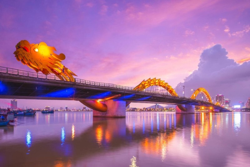 Dragon Bridge in Da Nang, Vietnam during sunset, beautifully illuminated with vibrant colors reflecting in the river.