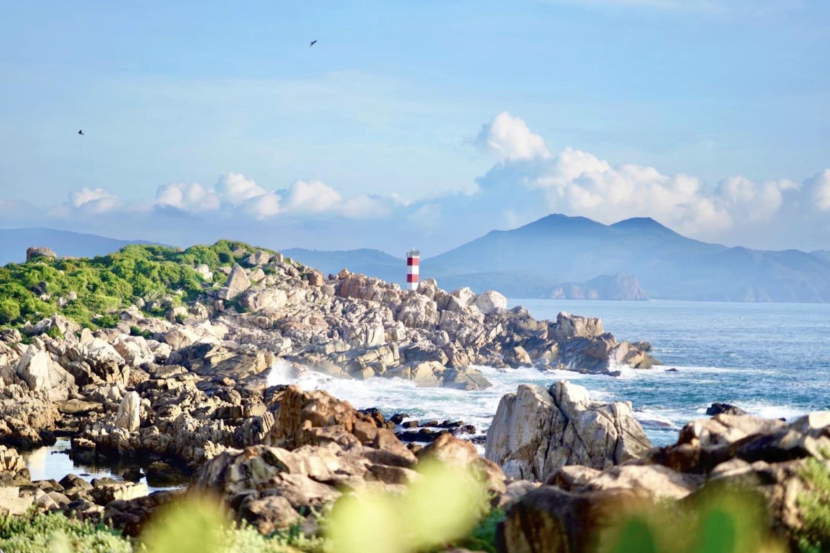 Scenic view of Ganh Den Lighthouse in Quang Ngai with rocky shores and distant mountains.