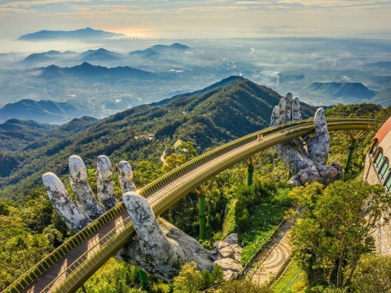 The Golden Bridge held by two giant stone hands at Ba Na Hills, Da Nang, Vietnam with a scenic mountain backdrop.