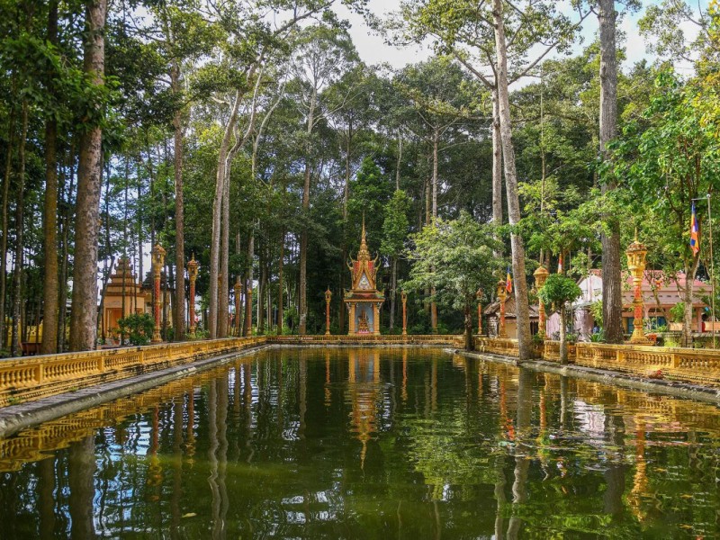 Golden Khmer temple reflecting on a pond in Tra Vinh, with intricate carvings.