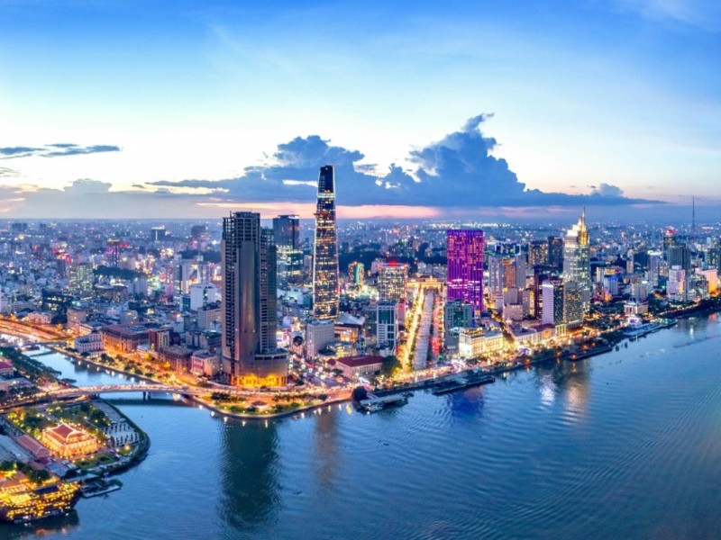 Aerial view of Ho Chi Minh City at dusk with the river and skyscrapers lit up.