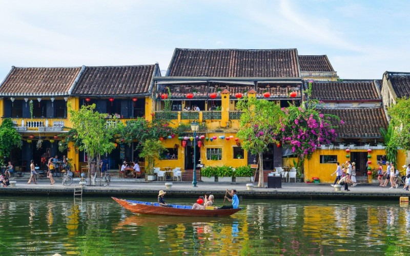 Hoi An Ancient Town riverside with historic architecture and tourists enjoying boat rides.