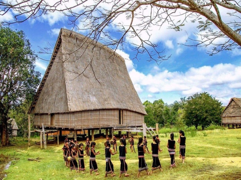 Traditional Kon Klor Communal House in Kon Tum, Vietnam, with a group of people dancing around