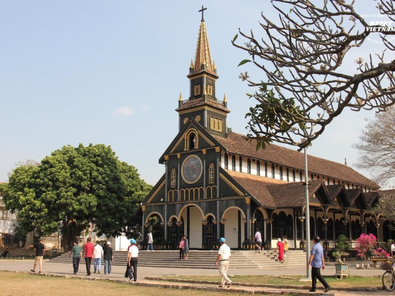 The historic Kon Tum Wooden Church in Vietnam, with visitors exploring the grounds