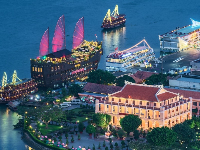 Nha Rong Wharf in Ho Chi Minh City lit up at night, with traditional boats in the harbor.