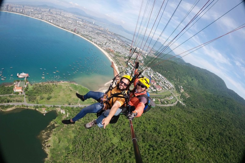 Paragliders soaring above Son Tra Peninsula in Da Nang, Vietnam with scenic views of the coastline and greenery.