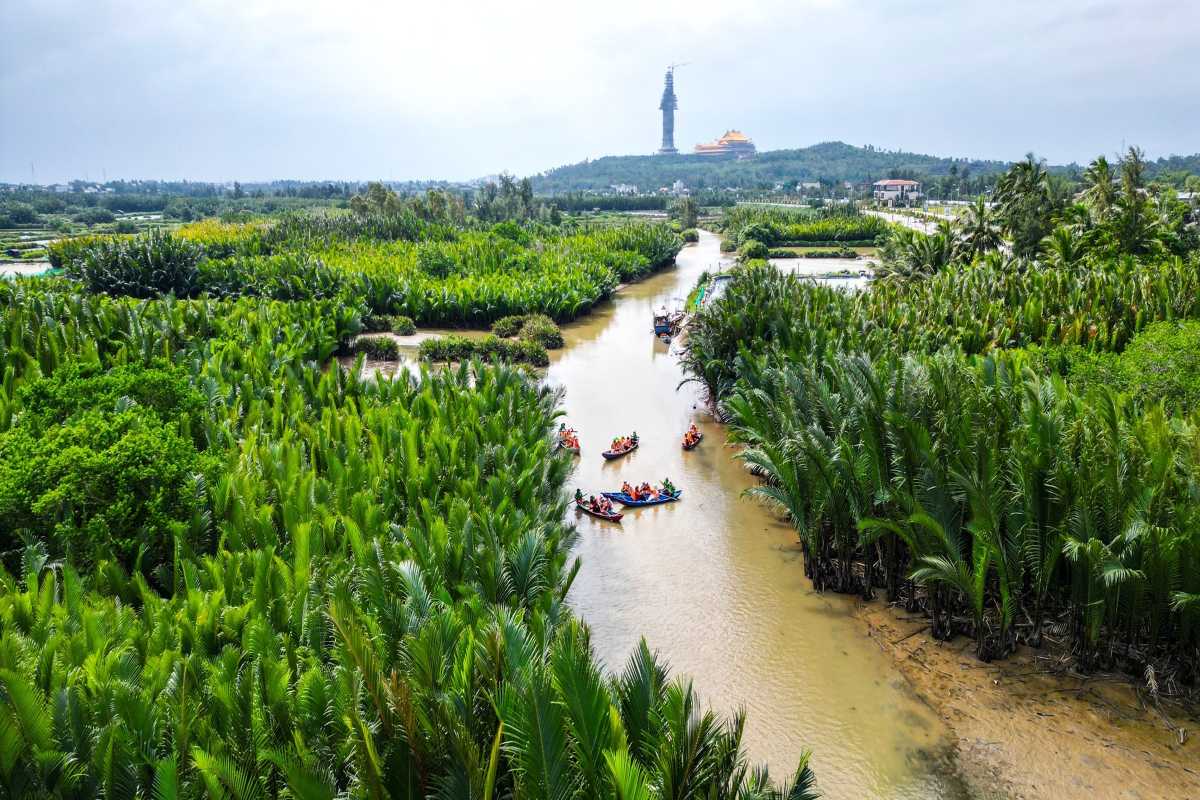Quang Ngai Palm River Boating and Mountain View Tourists boating along a palm-fringed river with mountain and statue view in Quang Ngai, Vietnam.
