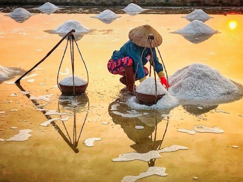 Worker gathering salt at Sa Huynh Salt Field in Quang Ngai at sunset.