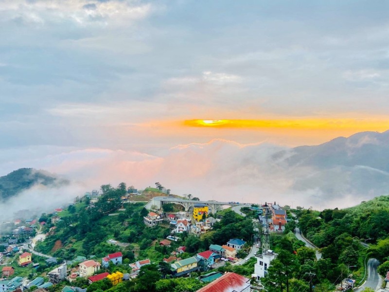 Sunrise view over the mountainous town of Tam Dao, with colorful houses and a cloud-filled valley.