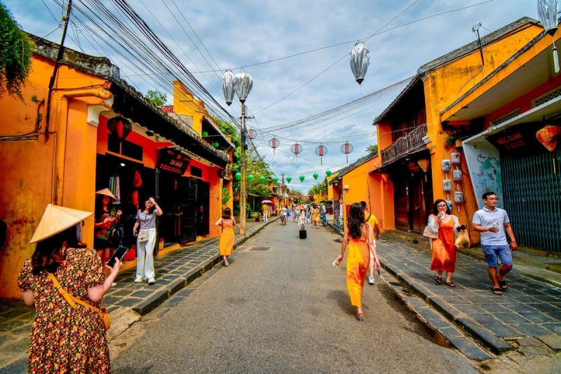 Tourists walking along a colorful street in Hoi An Ancient Town, showcasing the lively culture and traditional yellow-walled houses.