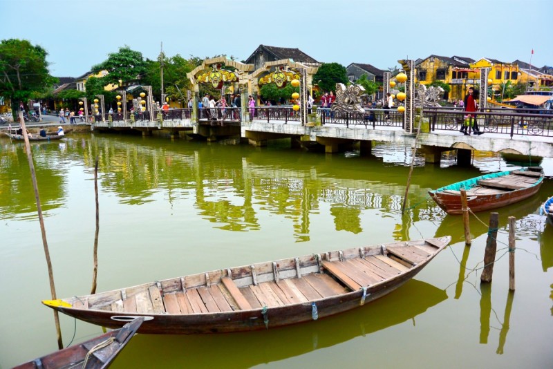 A traditional bridge in Hoi An Ancient Town, surrounded by scenic river views and tourists exploring the heritage site.