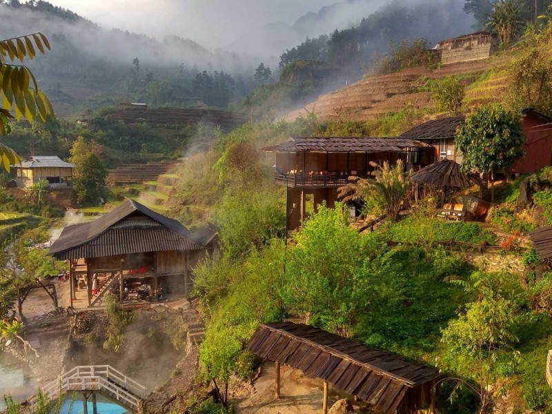 Steam rising from a traditional homestay at Tram Tau Hot Spring, surrounded by terraced fields.