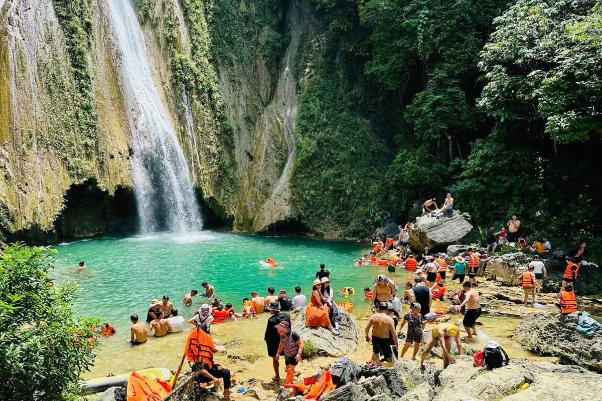 Tuyen Quang Mo Waterfall Natural Swimming Spot Mo Waterfall in Tuyen Quang with turquoise pool and visitors swimming surrounded by lush greenery and rocky cliffs
